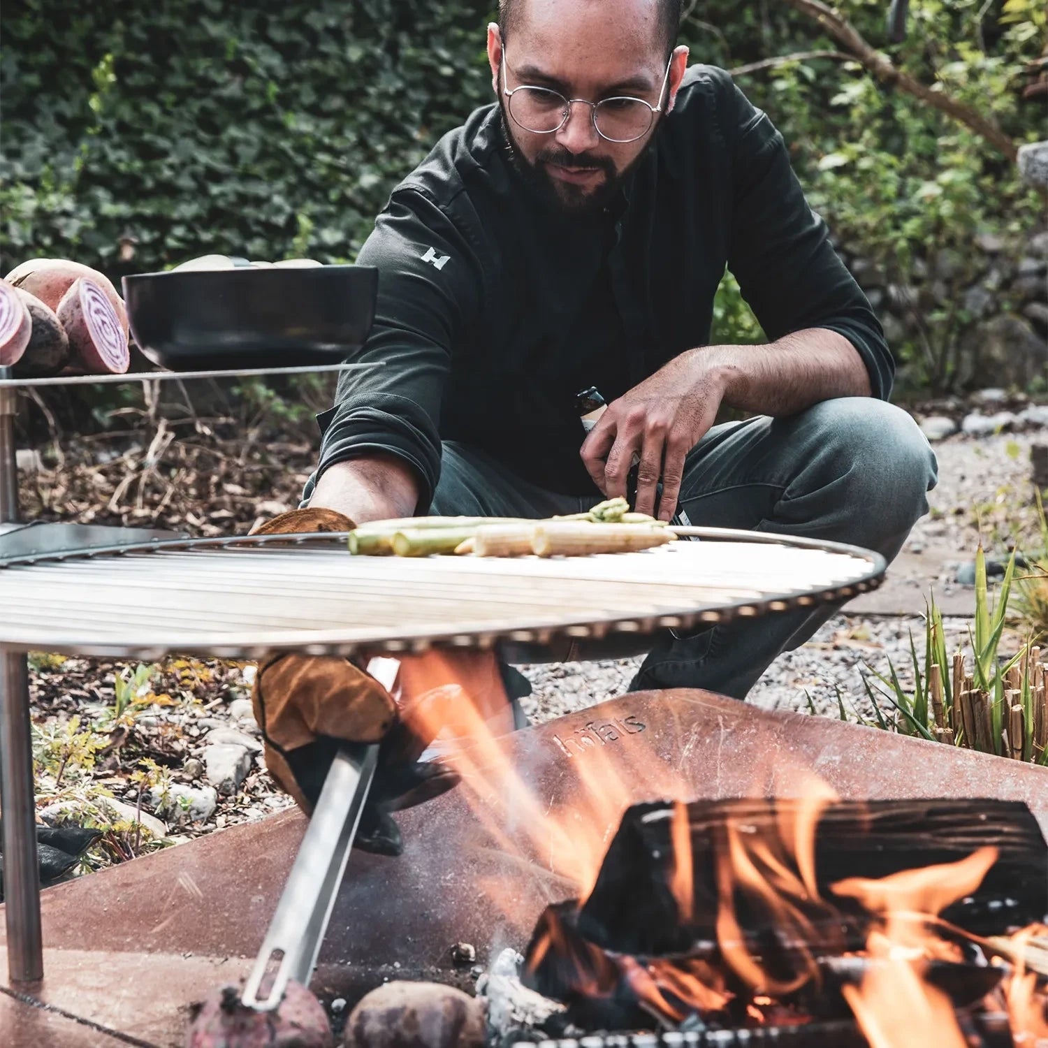 Höfats TRIPLE 120 Fire Pit in Corten Steel with burning logs, placed on a white surface.